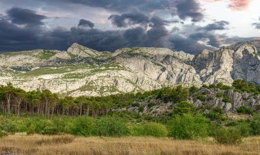 Kayalık dağ manzarası ve zıt bulutlu gökyüzü. Hırvatistan