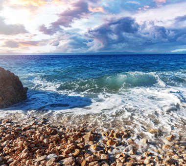 Deniz sörfü. Gün batımında taştan bir plajı olan resim gibi bir sahil..