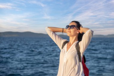 Mutlu genç kadın turist gün batımında deniz kenarında.