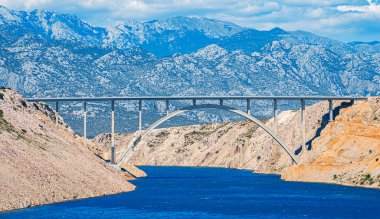 Dağların arka planına uzanan bir yolu olan beton kemer köprüsü.