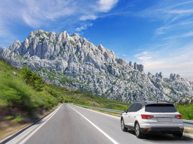 Güneşli bir günde, beyaz bir araba kayalık dağların arka planına doğru yol alır..
