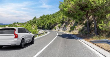 Güneşli bir günde, beyaz bir araba kayalık dağların arka planına doğru yol alır..