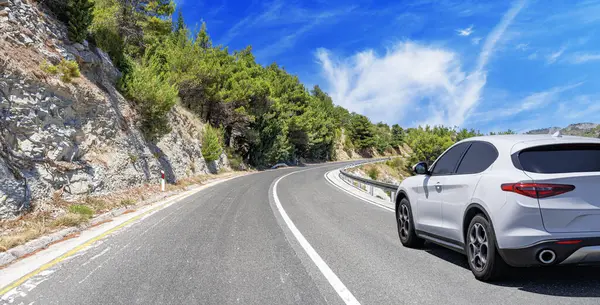 阳光灿烂的一天 一辆白色的汽车在岩石山的背景下沿着公路行驶 图库照片