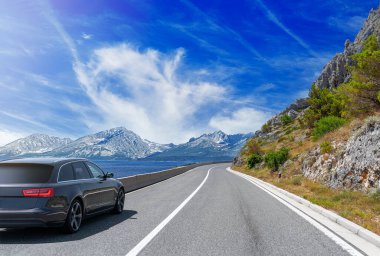 Siyah araba güneşli bir yaz gününde deniz kıyısı boyunca yol alır..
