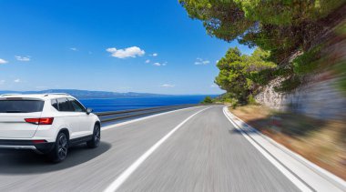 Güneşli bir yaz gününde deniz kıyısı boyunca beyaz bir araba sürüyor..