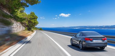 Mavi araba güneşli bir yaz gününde deniz kıyısı boyunca yol alır..