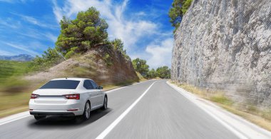 Güneşli bir günde, beyaz bir araba kayalık dağların arka planına doğru yol alır..