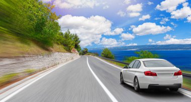 Güneşli bir yaz gününde deniz kıyısı boyunca beyaz bir araba sürüyor..
