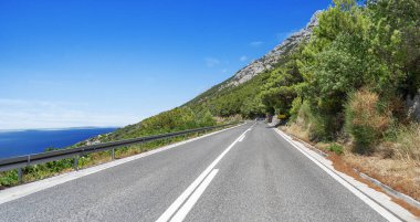 Güneşli bir yaz gününde deniz kıyısı boyunca beyaz bir araba sürüyor..