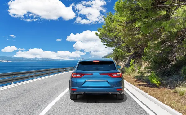 Blue car drives along the sea coastline on a sunny summer day.