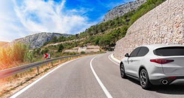 Güneşli bir günde, beyaz bir araba kayalık dağların arka planına doğru yol alır..