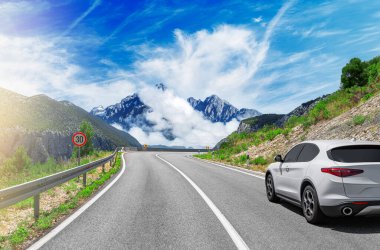 Güneşli bir günde, beyaz bir araba kayalık dağların arka planına doğru yol alır..