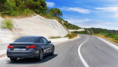 Güneşli bir günde, beyaz bir araba kayalık dağların arka planına doğru yol alır..