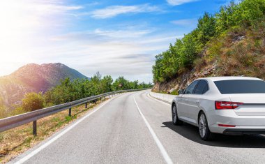 Güneşli bir günde, beyaz bir araba kayalık dağların arka planına doğru yol alır..