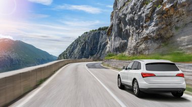 Güneşli bir günde, beyaz bir araba kayalık dağların arka planına doğru yol alır..