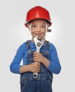 Güvenlik kaskı takmış, arka planda bir aleti olan küçük bir kız işçi..