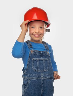 Güvenlik kaskı takmış, arka planda bir aleti olan küçük bir kız işçi..