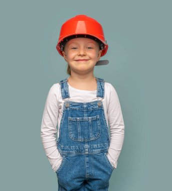 Mavi arka planda bir aleti olan kasklı küçük bir kız işçi..