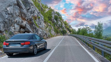 Güneşli bir günde, beyaz bir araba kayalık dağların arka planına doğru yol alır..