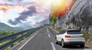 Beyaz araba bir yaz günü kayalık dağların arka planına doğru yol alır..