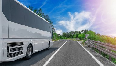 Beyaz bir otobüs asfalt yolun her iki tarafındaki yemyeşil ağaçlar ve bitkilerle çevrili bulutlu bir ekosistem boyunca iniyor.