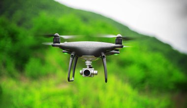 Yağmurda bir ormanın arka planında kamerayla uçan siyah bir dron..