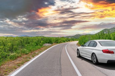 Güneşli bir günde, beyaz bir araba kayalık dağların arka planına doğru yol alır..