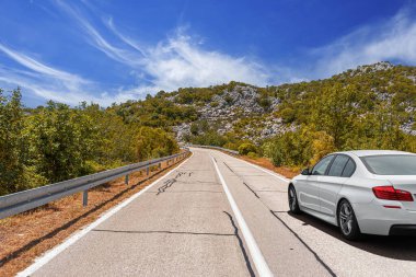 Güneşli bir günde, beyaz bir araba kayalık dağların arka planına doğru yol alır..