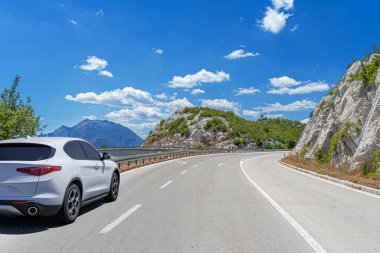 Güneşli bir günde, beyaz bir araba kayalık dağların arka planına doğru yol alır..