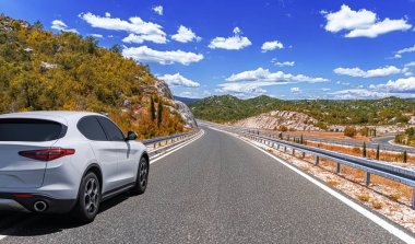 Güneşli bir günde, beyaz bir araba kayalık dağların arka planına doğru yol alır..