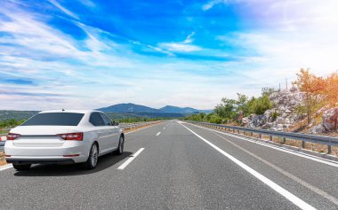 Güneşli bir günde, beyaz bir araba kayalık dağların arka planına doğru yol alır..