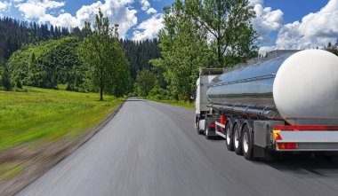Yakıt kamyonu güzel bir yolda. Gümüş bir tank kamyonu yakıt taşıyor..