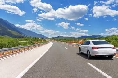 Güneşli bir günde, beyaz bir araba kayalık dağların arka planına doğru yol alır..