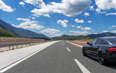 Güneşli bir günde, siyah bir araba kayalık dağların arka planına doğru yol alır..