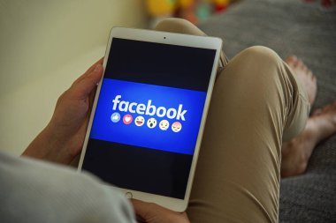 Uzhgorod, Ukrayna - 06 Eylül 2020: Bir kadın kanepede yatarken sosyal ağda Facebook tablet kullanıyor.