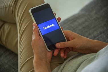 Uzhgorod, Ukrayna - 06 Eylül 2020: Bir kadın kanepede yatarken sosyal ağda Facebook tablet kullanıyor.
