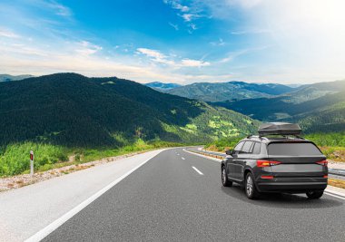 Yolculuk arabası, güneşli bir günde, kayalık dağların arka planına karşı otoyol boyunca gider..