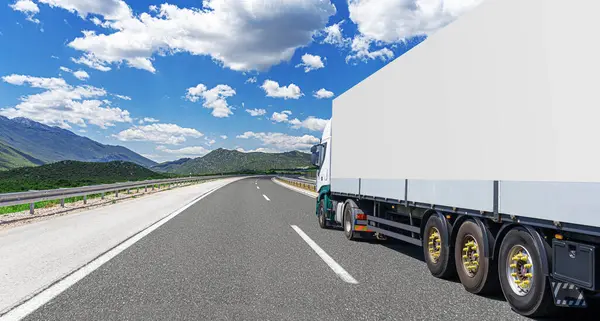 Stock image A white truck transports cargo along the highway against the backdrop of a mountain landscape.