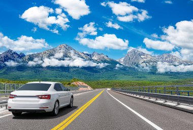 Güneşli bir günde, beyaz bir araba kayalık dağların arka planına doğru yol alır..