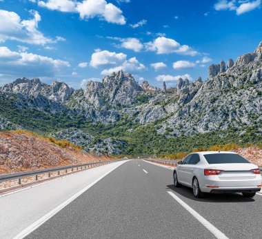 Güneşli bir günde, beyaz bir araba kayalık dağların arka planına doğru yol alır..