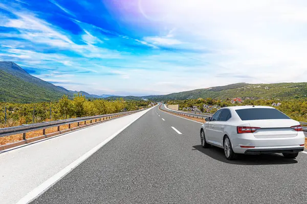 Güneşli bir günde, beyaz bir araba kayalık dağların arka planına doğru yol alır..