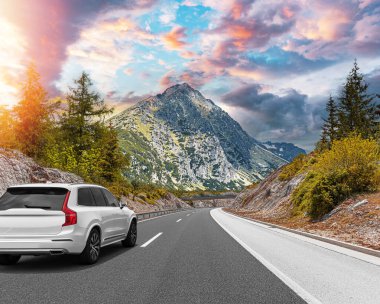 Güneşli bir günde, beyaz bir araba kayalık dağların arka planına doğru yol alır..