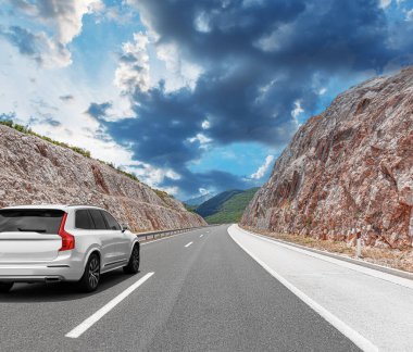 Güneşli bir günde, beyaz bir araba kayalık dağların arka planına doğru yol alır..