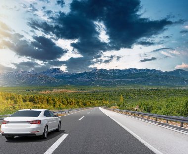Güneşli bir günde, beyaz bir araba kayalık dağların arka planına doğru yol alır..