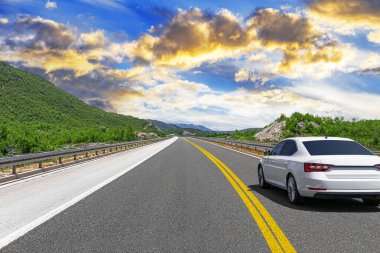 Güneşli bir günde, beyaz bir araba kayalık dağların arka planına doğru yol alır..