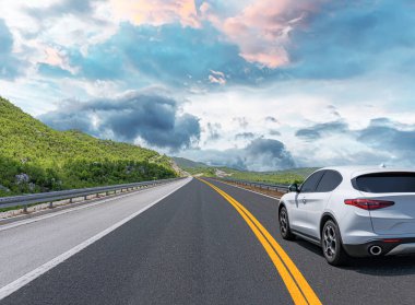 Güneşli bir günde, beyaz bir araba kayalık dağların arka planına doğru yol alır..