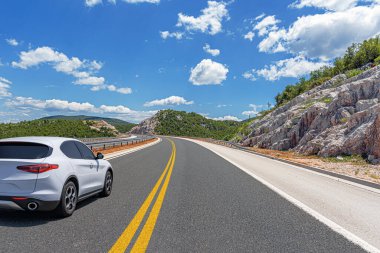 Güneşli bir günde, beyaz bir araba kayalık dağların arka planına doğru yol alır..