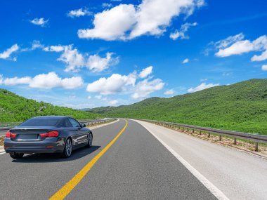 Gri bir araba güneşli bir günde otoyol boyunca kayalık dağların arka planına doğru gidiyor..
