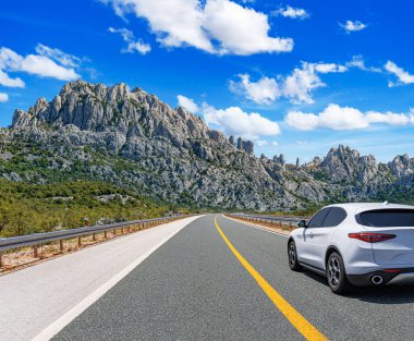 Güneşli bir günde, beyaz bir araba kayalık dağların arka planına doğru yol alır..