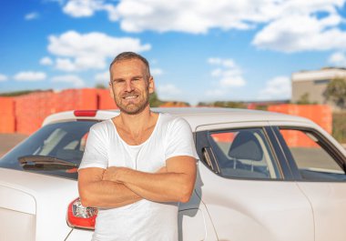 Beyaz bir arabanın arka planında poz veren çekici genç bir adam..